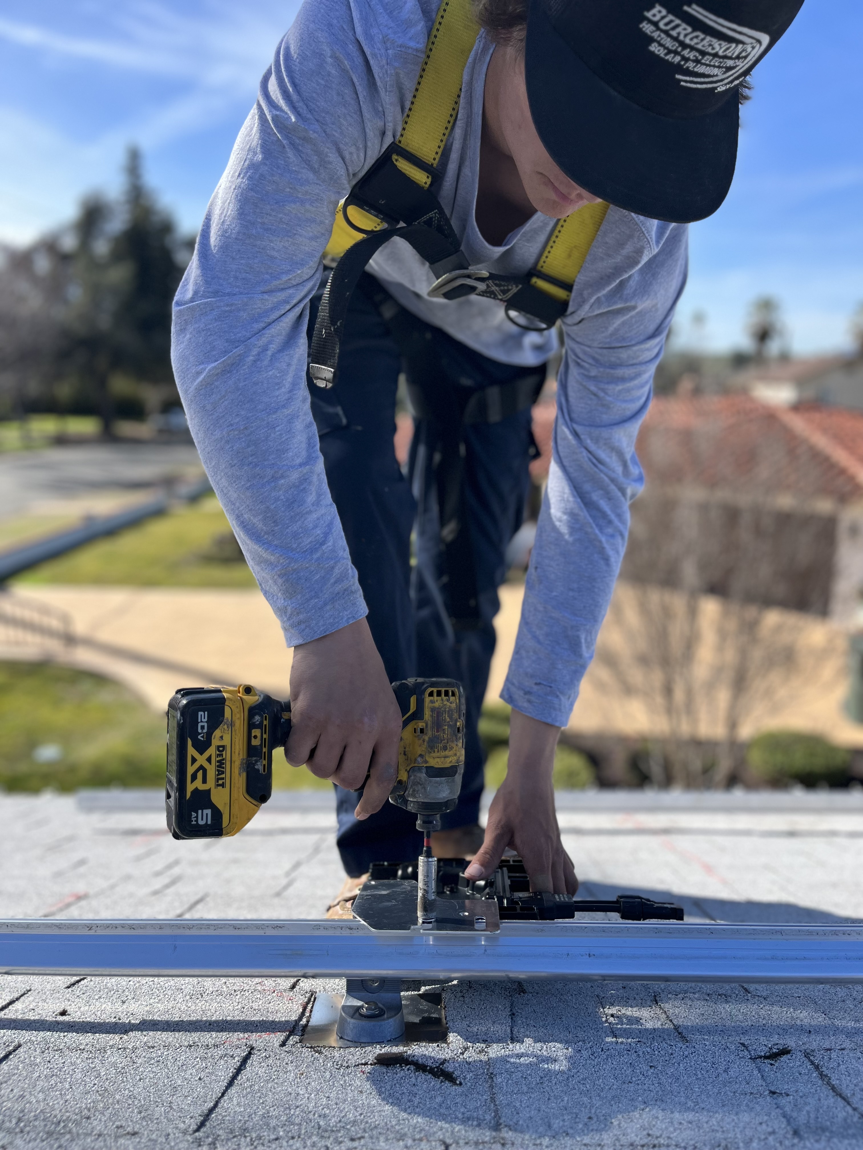 Burgeson’s technician installing solar panel mounting equipment on a California rooftop with safety harness and drill.