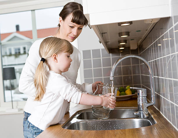 Mother and daughter over sink pouring glass of water